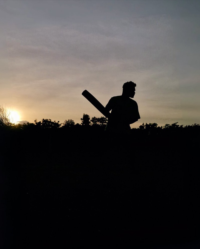 Silhouette of an unidentified cricket batter holding a bat at sunset